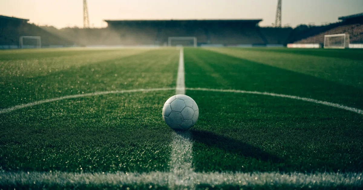 Uma bola de futebol no ponto central de um relvado, à luz da manhã