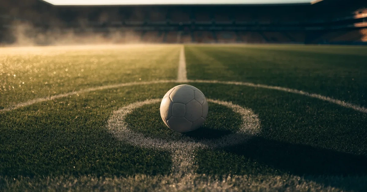 Uma bola de futebol no ponto central de um relvado, à luz da manhã