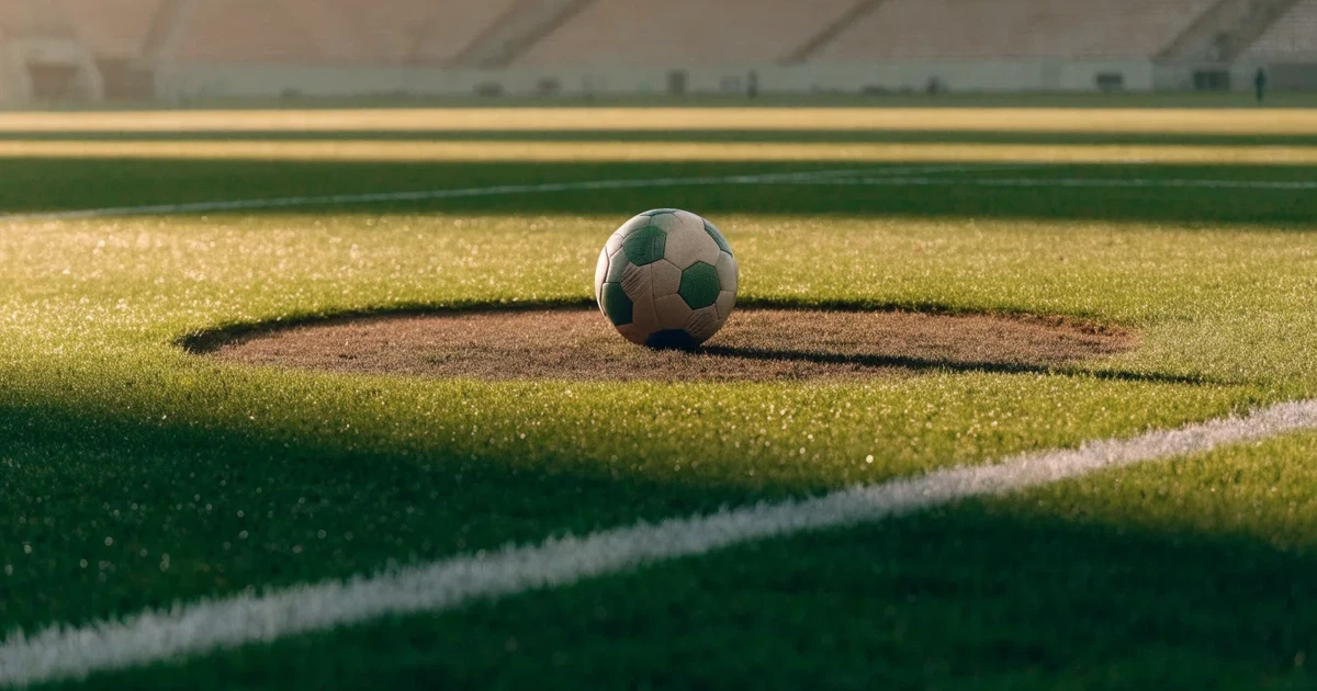 Uma bola de futebol no ponto central de um relvado, à luz da manhã
