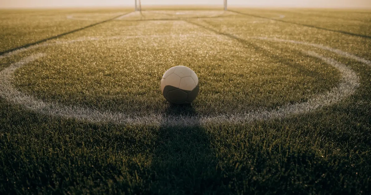 Uma bola de futebol no ponto central de um relvado, à luz da manhã