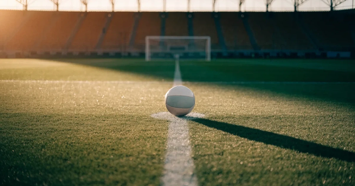 Uma bola de futebol no ponto central de um relvado, à luz da manhã